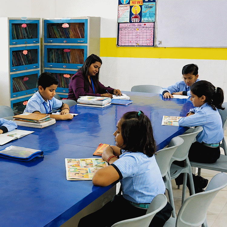 A teacher and students reading books around a large table in the school library